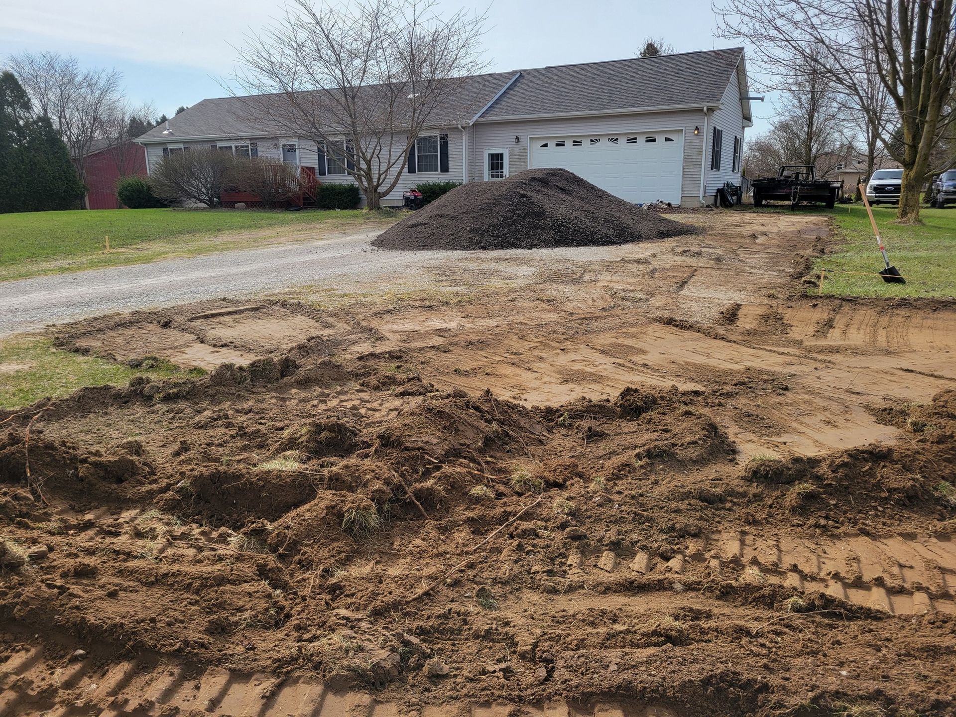 Backyard excavation with dirt piles in front of a house and garage driveway