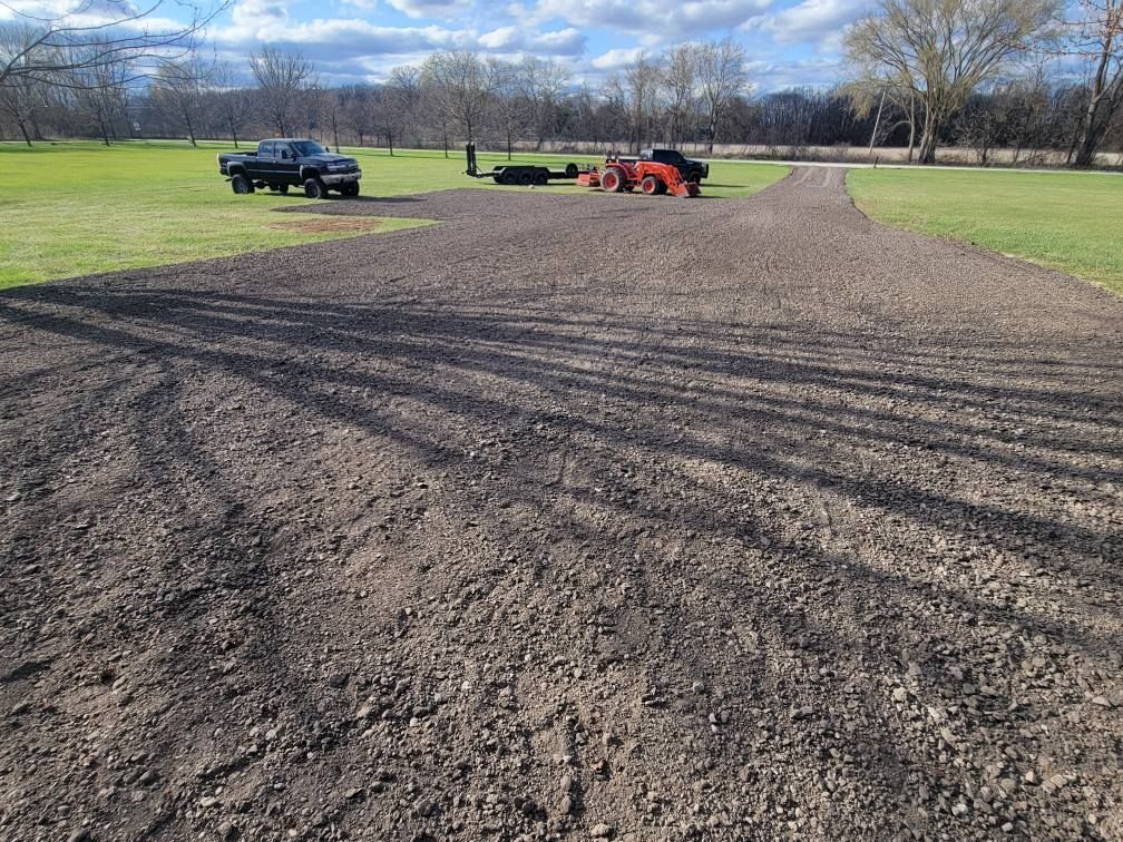 Gravel path in a park with a black truck and red tractor in the distance under a clear sky