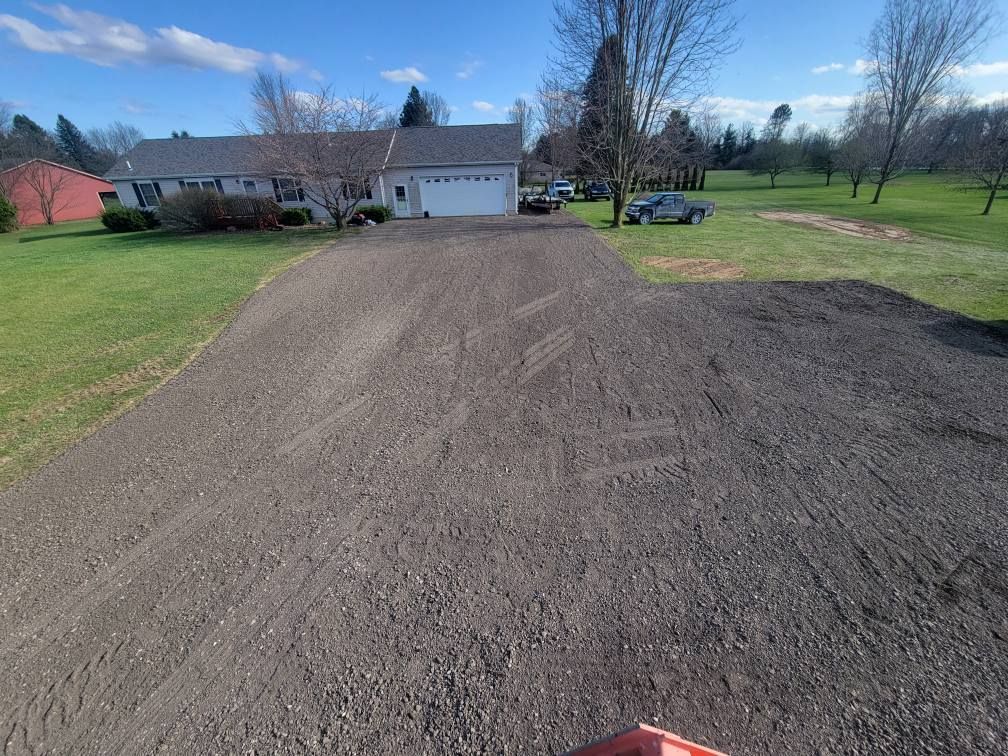 Gravel driveway leading to a house in a rural yard on a sunny day