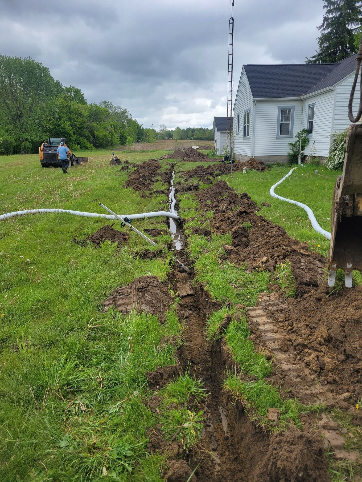 Storm-damaged yard beside a white house, with uprooted ground and hoses stretched across muddy grass.