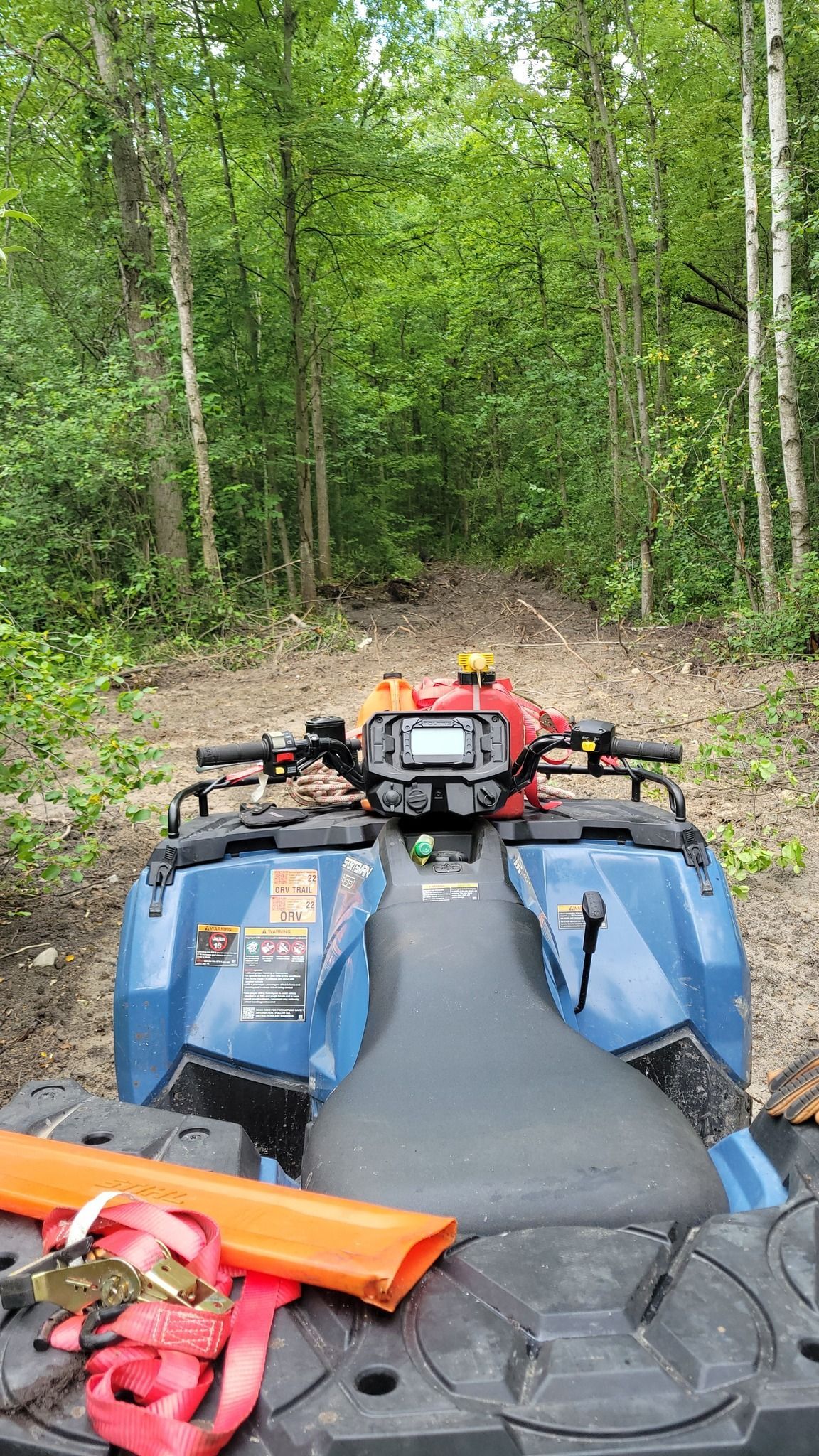 Blue ATV parked on a narrow forest trail with dense green trees ahead