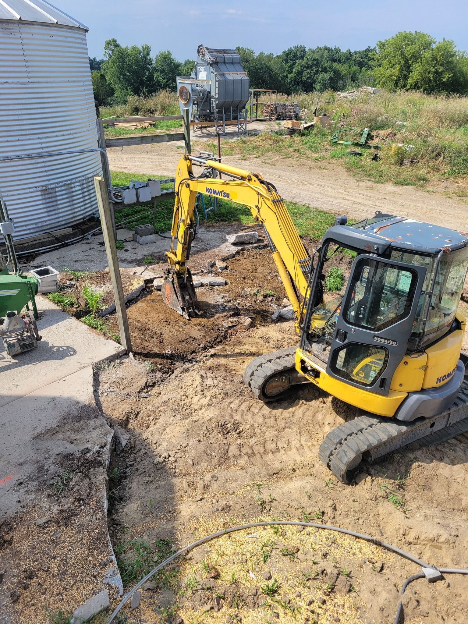 Yellow excavator digging dirt beside a white building in a yard