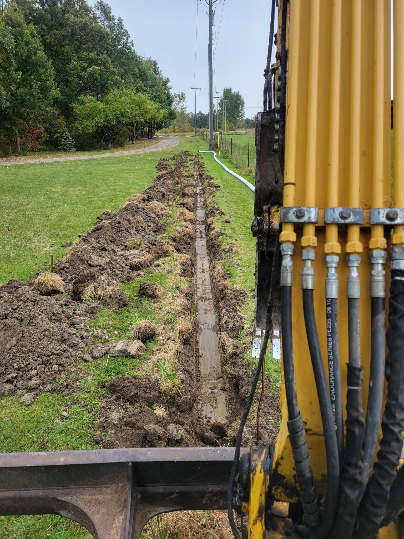 Yellow drilling rig beside a narrow muddy trench along a grassy roadside