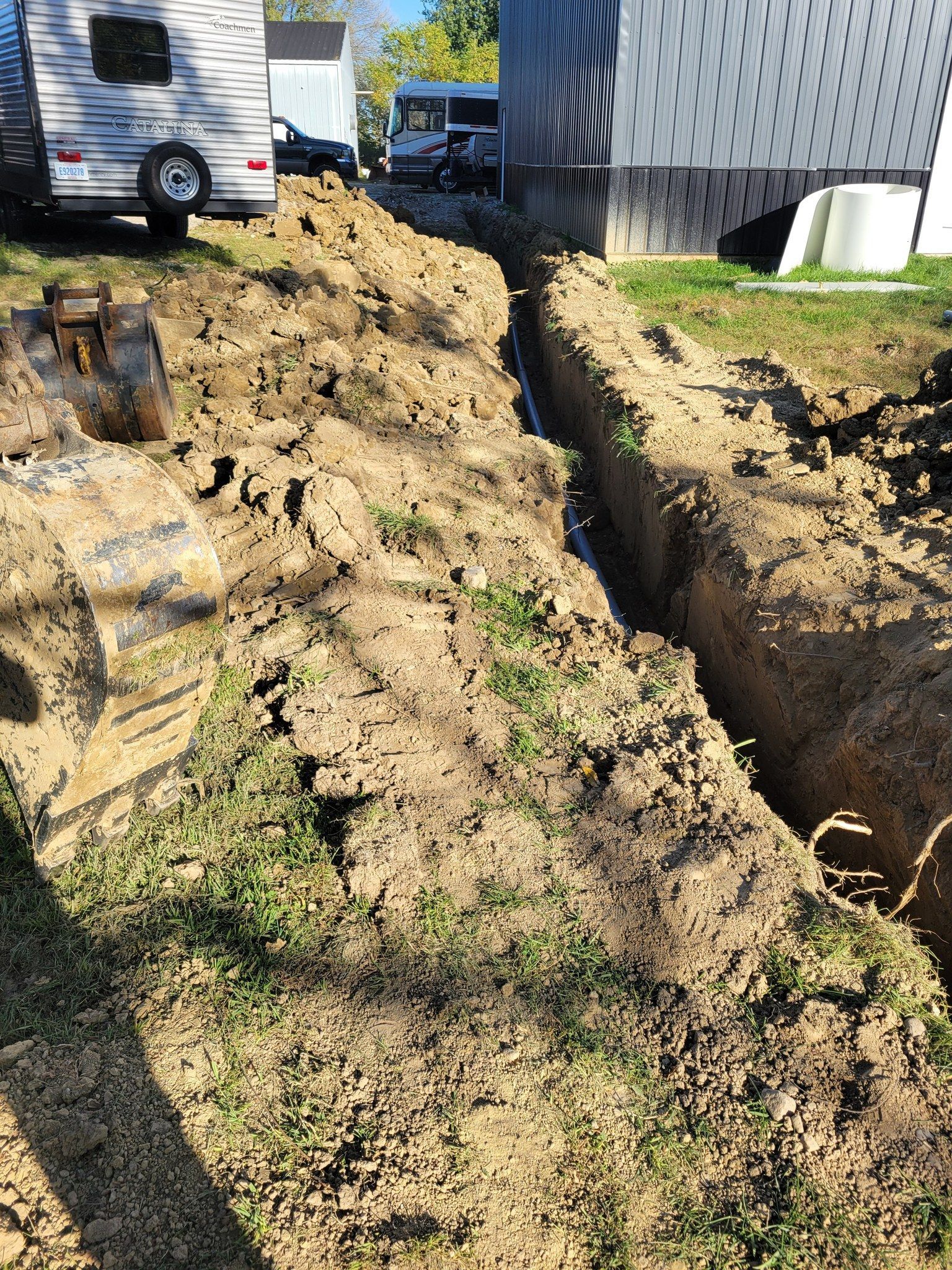 Freshly dug trench along a house beside a muddy yard and trailers