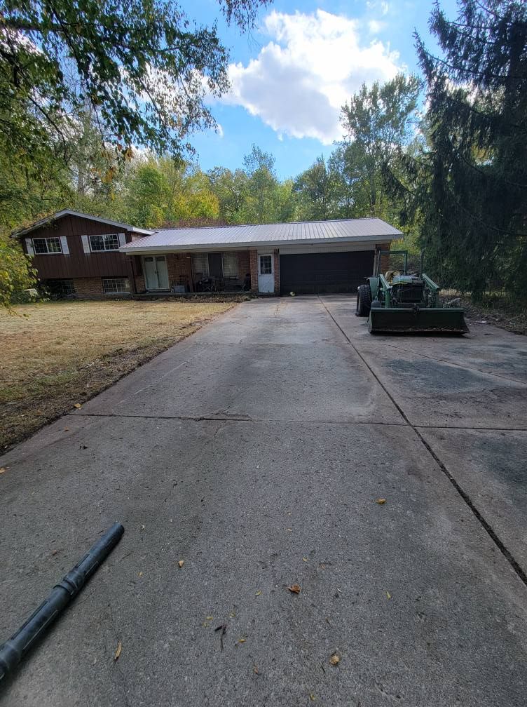 Long driveway leading to a suburban house with a garage and trees under a partly cloudy sky
