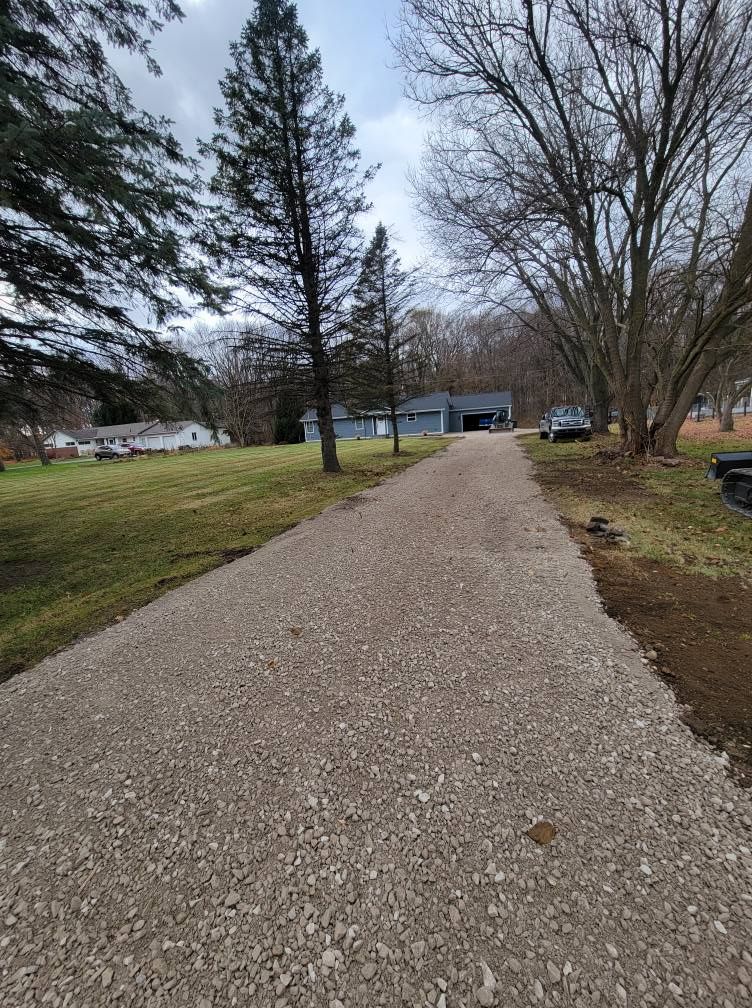 Gravel driveway leading to a house and garage through a grassy yard with leafless trees.