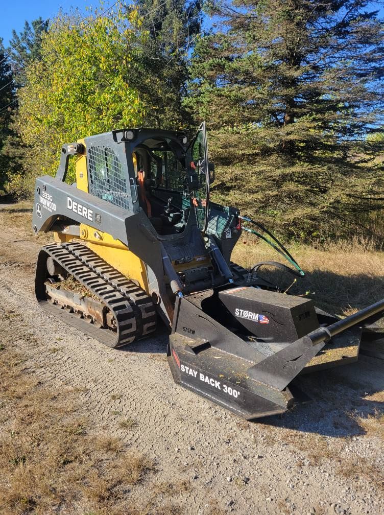 Yellow and black track loader parked on a gravel path beside trees and dry grass