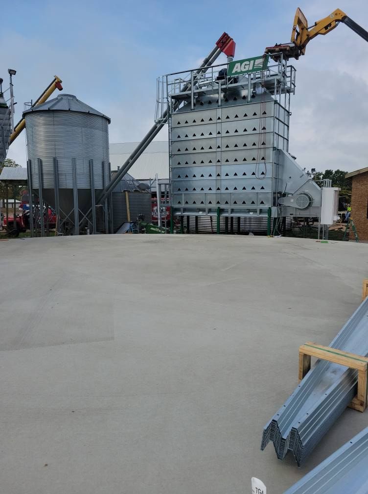 Industrial grain facility with silos and conveyors, featuring a large metal storage building and equipment outdoors