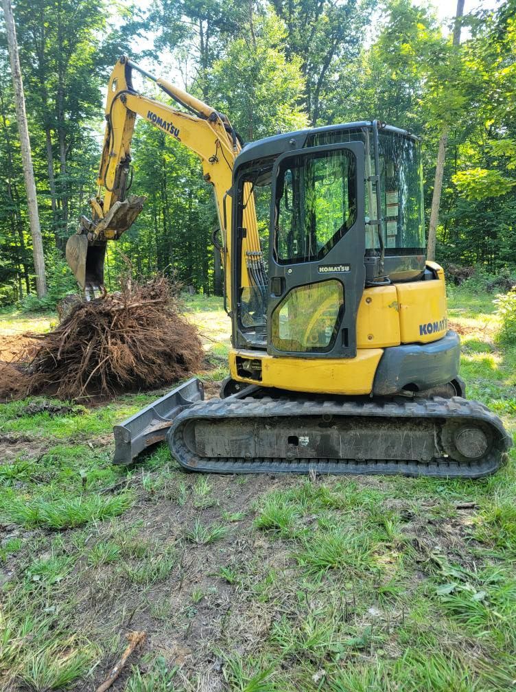 Yellow excavator lifting a pile of roots in a wooded clearing