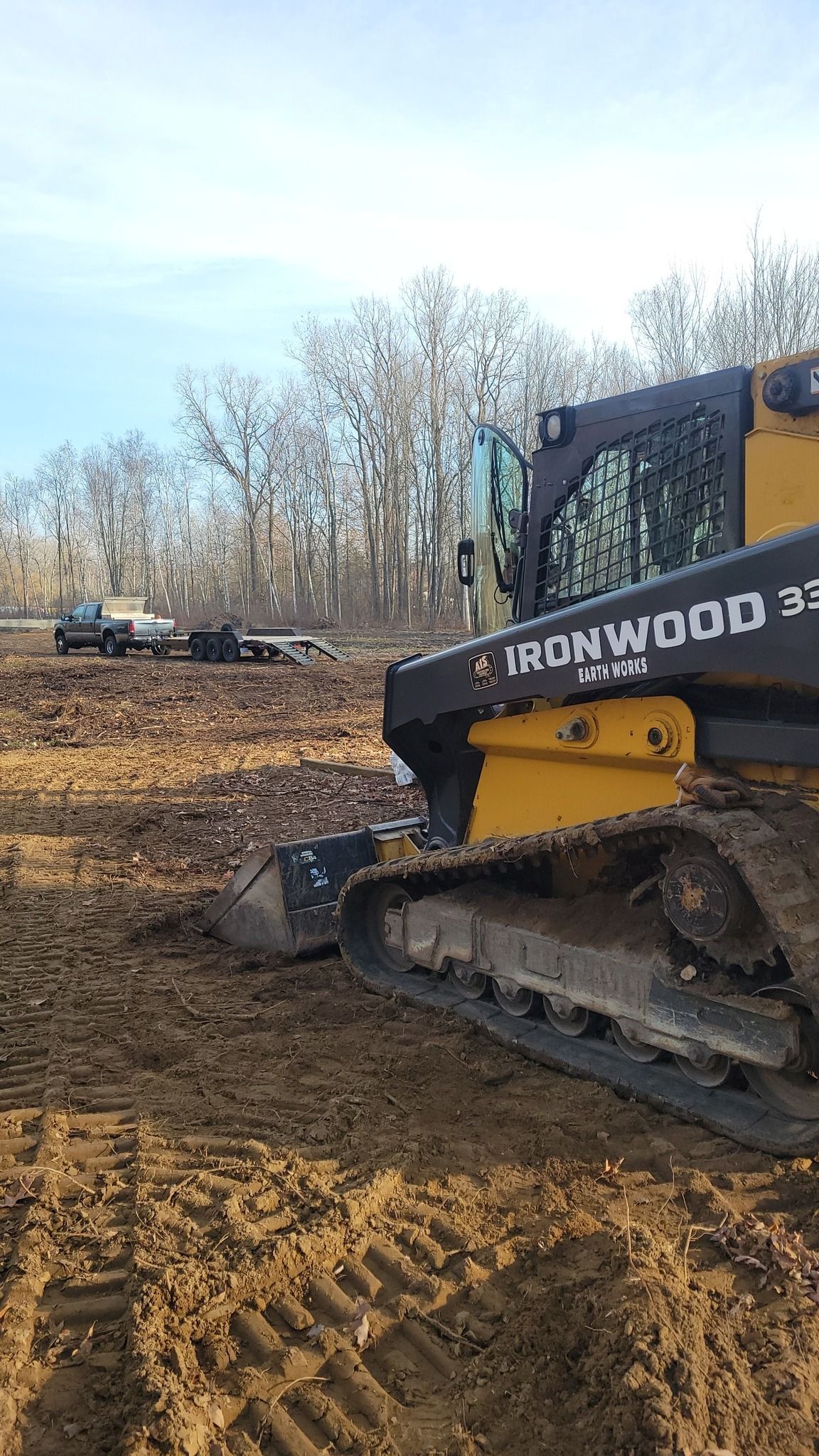 Yellow-and-black skid steer on muddy ground at a construction site with bare trees in the background