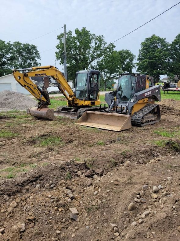 Two construction machines parked on a dirt lot, including a yellow excavator and a black bulldozer.