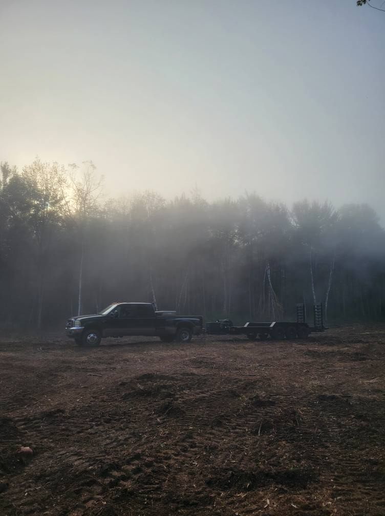 Black pickup truck parked on a muddy field at dawn, with mist and trees in the background.