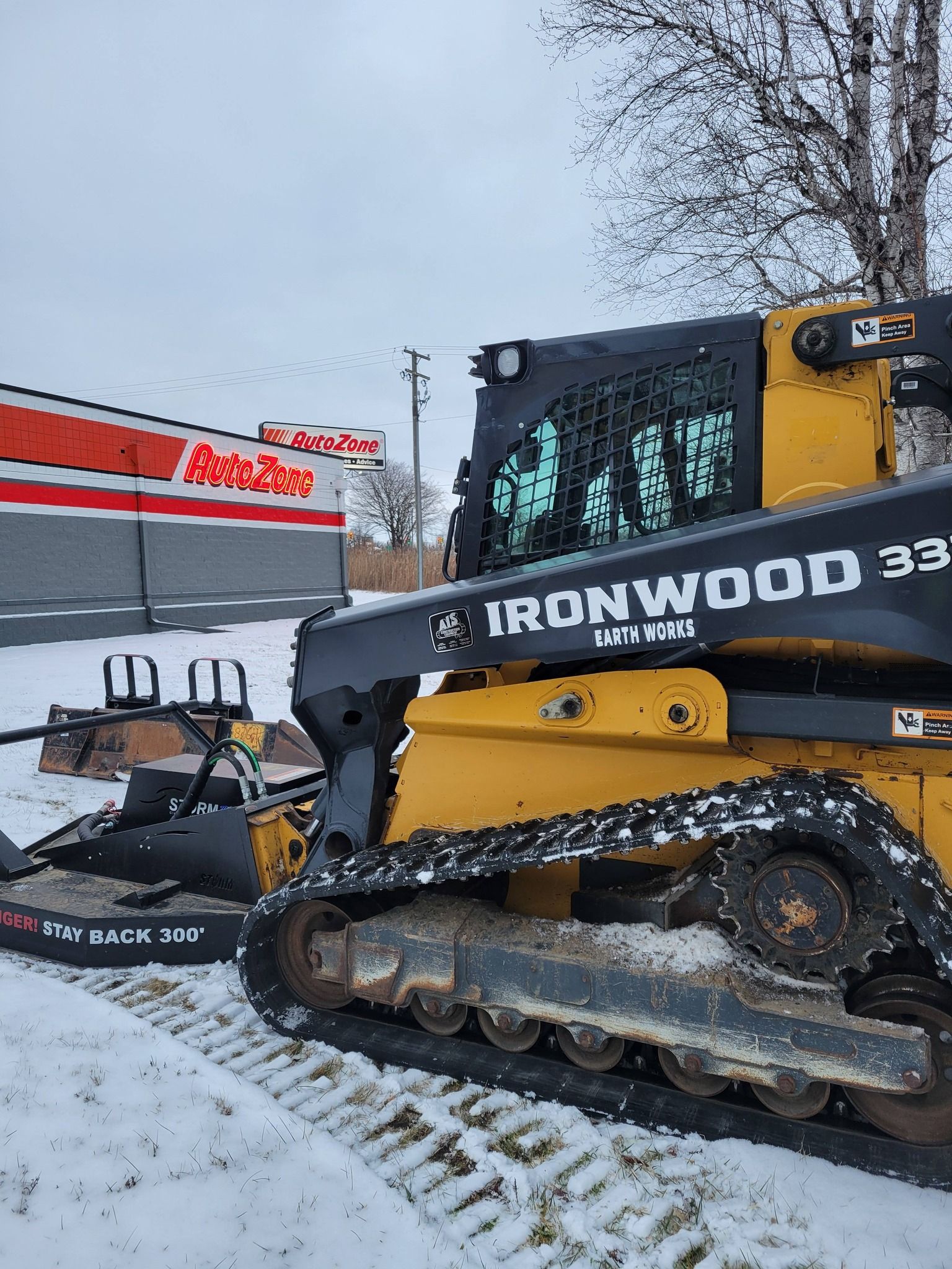 Yellow-and-black skid steer loader on snowy ground beside a building in winter
