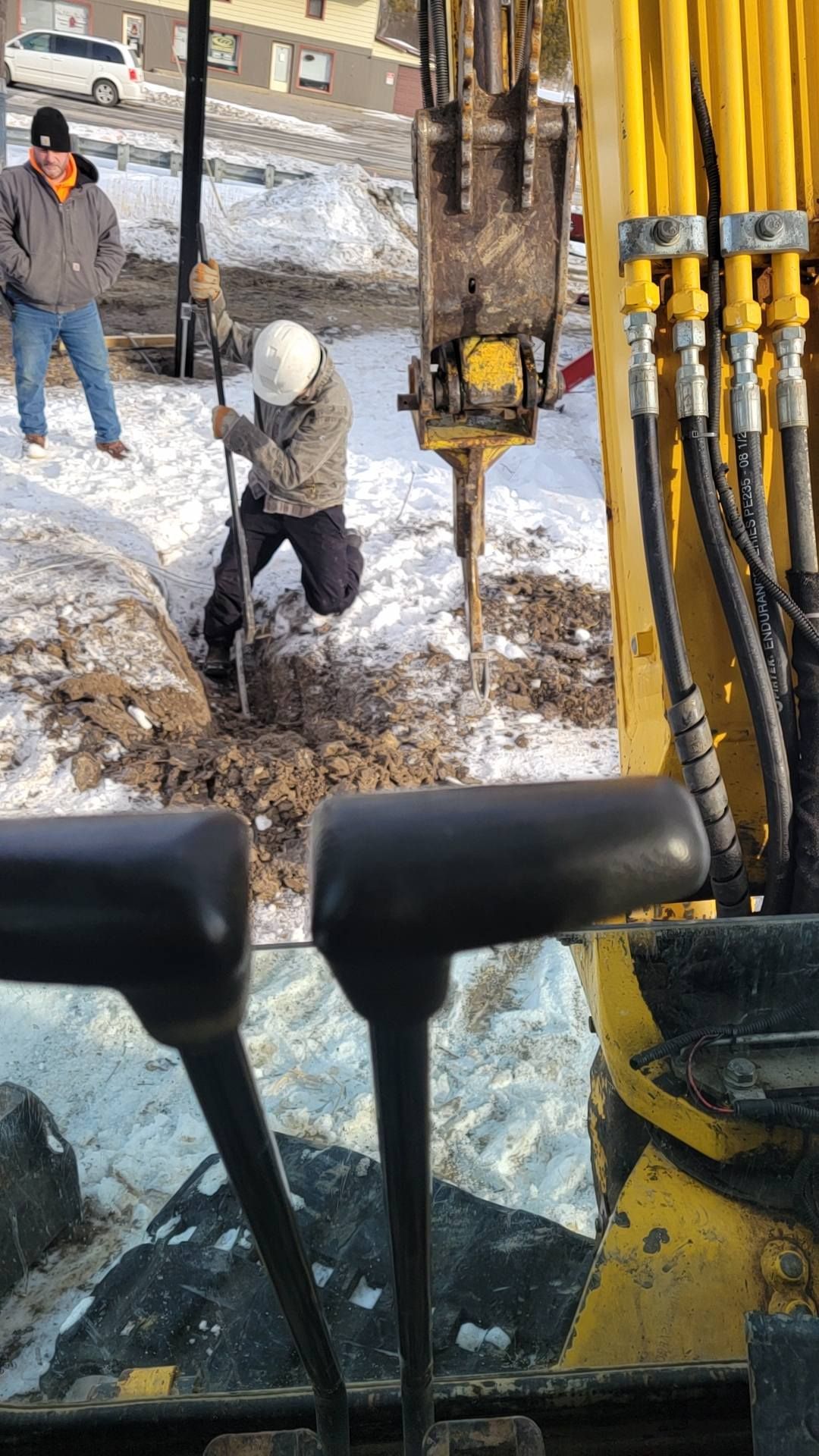 Construction workers drilling in a snowy site, viewed from inside heavy machinery cab.