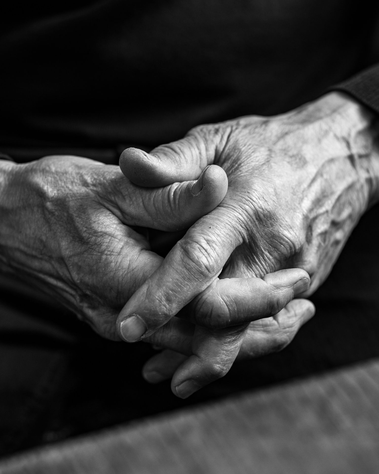 Black-and-white close-up of two clasped hands resting in a lap
