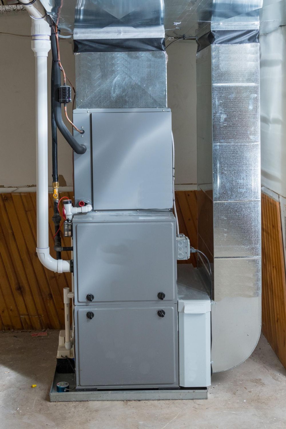 Indoor HVAC furnace and ductwork in a basement utility room, with silver insulated vents and white panels.