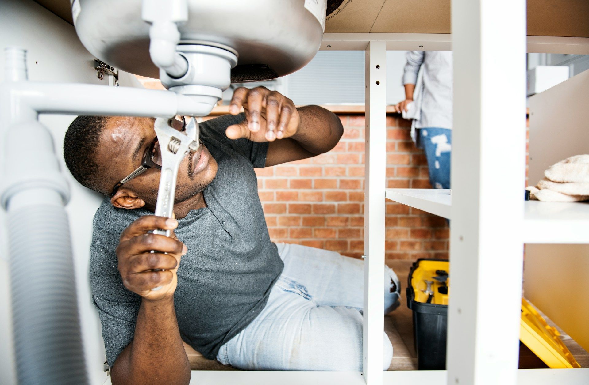 Plumber repairing a sink pipe under a bathroom vanity with a wrench