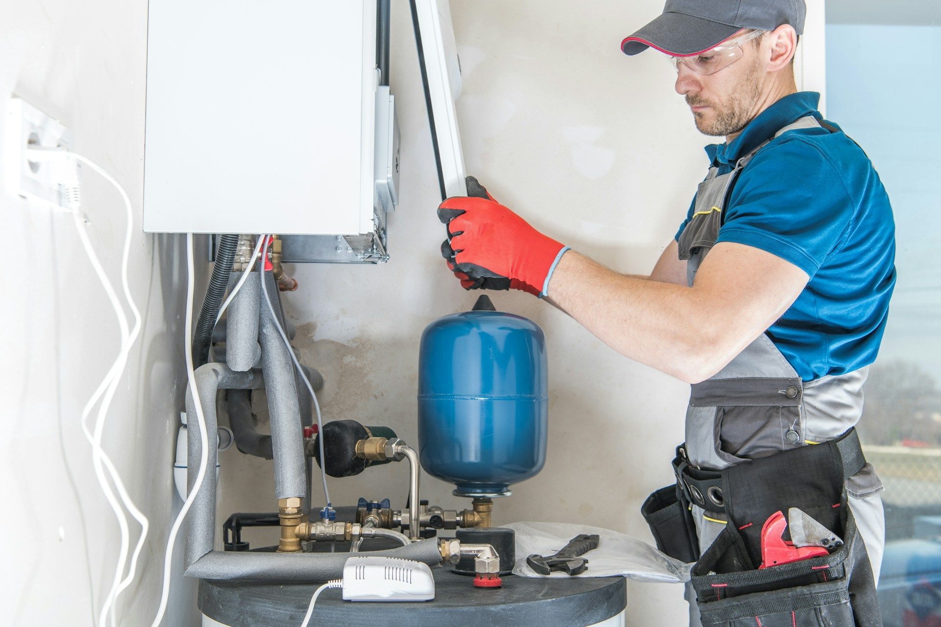 Technician in red gloves servicing a wall-mounted boiler with tools in a utility room.