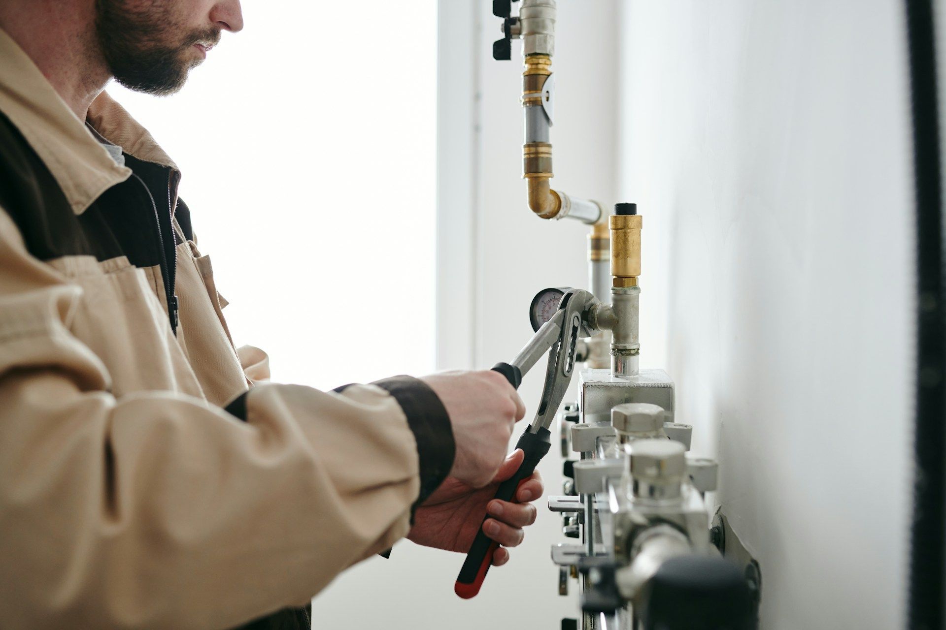Technician tightening a pipe fitting with pliers beside a wall-mounted boiler and pipes
