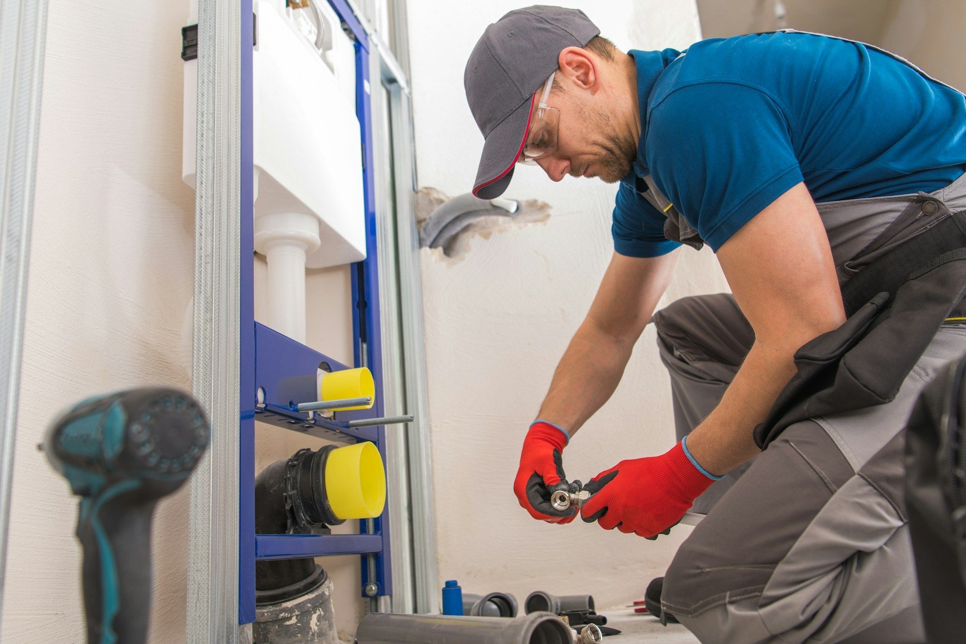 Plumber in red gloves installing pipes under a sink in a bathroom