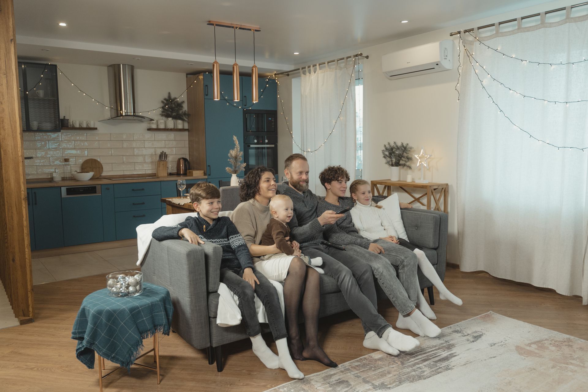 Family sitting on a gray couch in a bright living room, watching TV together