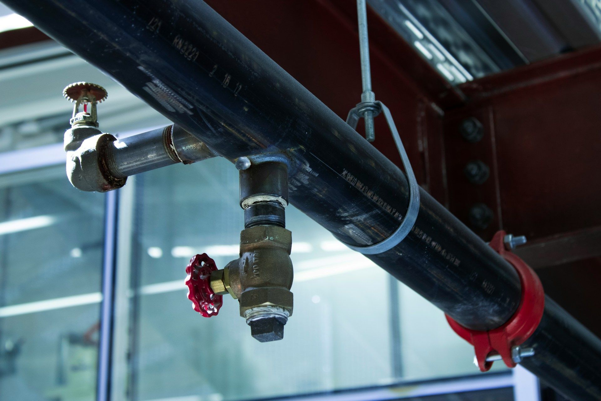Red fire sprinkler pipe with red valve and clear glass ceiling background