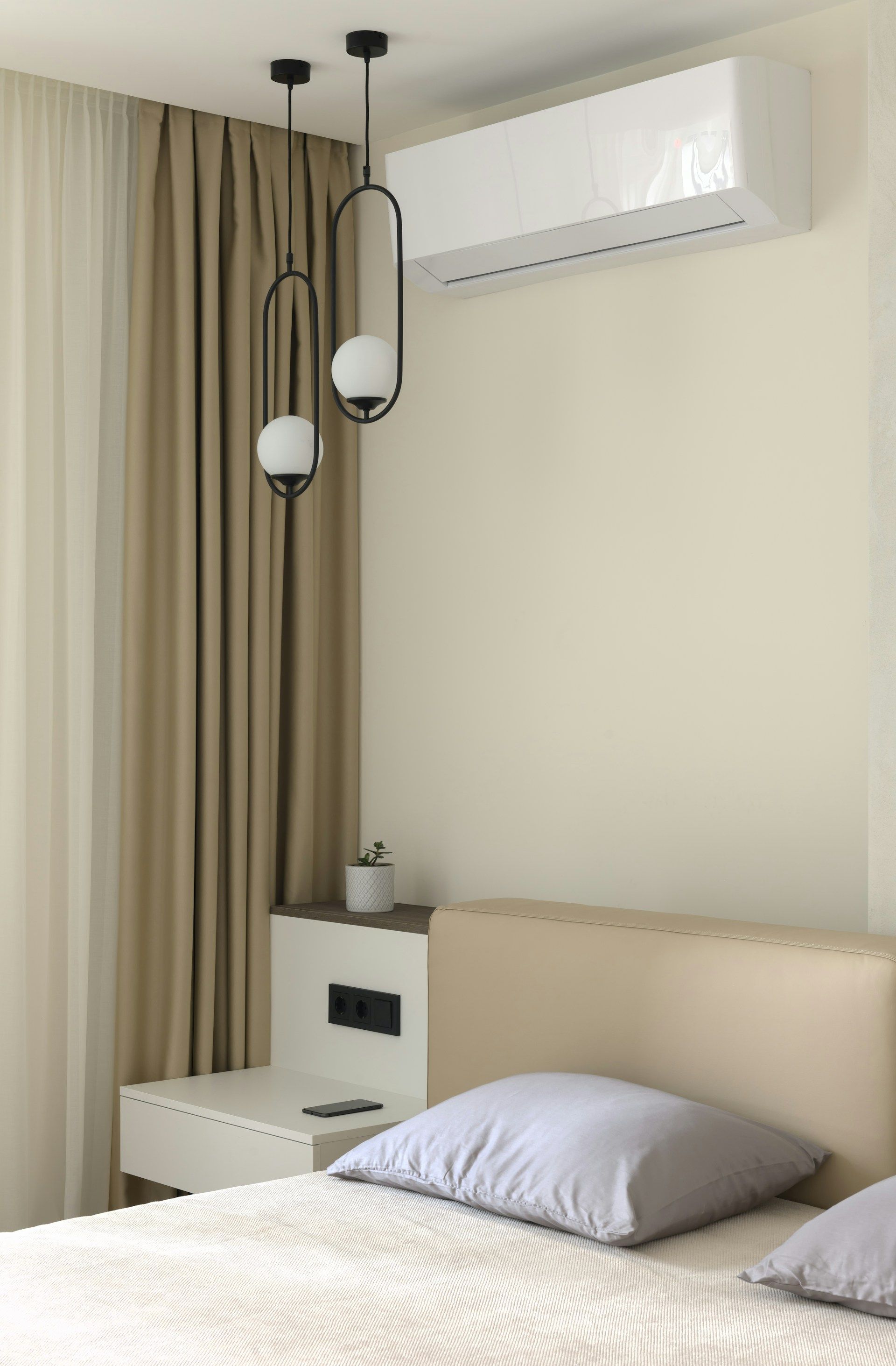 Minimal bedroom with beige walls, twin bed, nightstand, pendant lights, and wall-mounted air conditioner