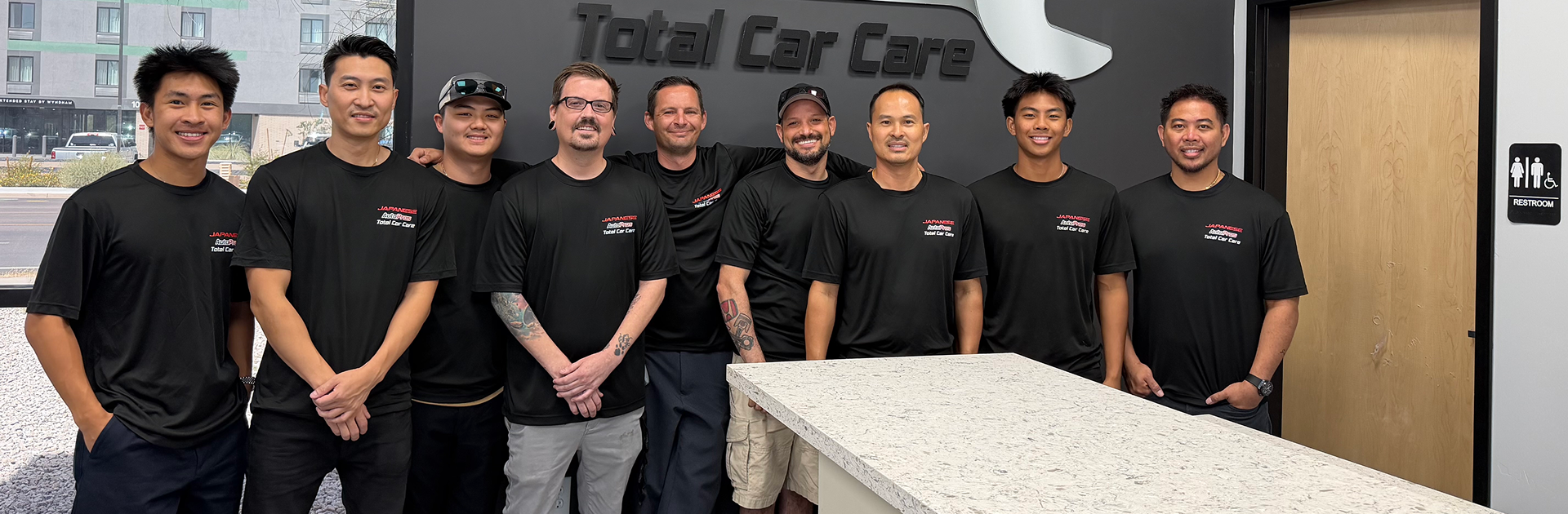 Seven employees in black shirts stand smiling in a car care shop lobby