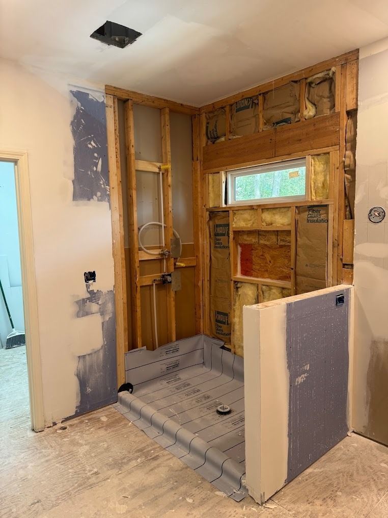 Bathroom under renovation with exposed wall studs, tiled shower base, and unfinished drywall.