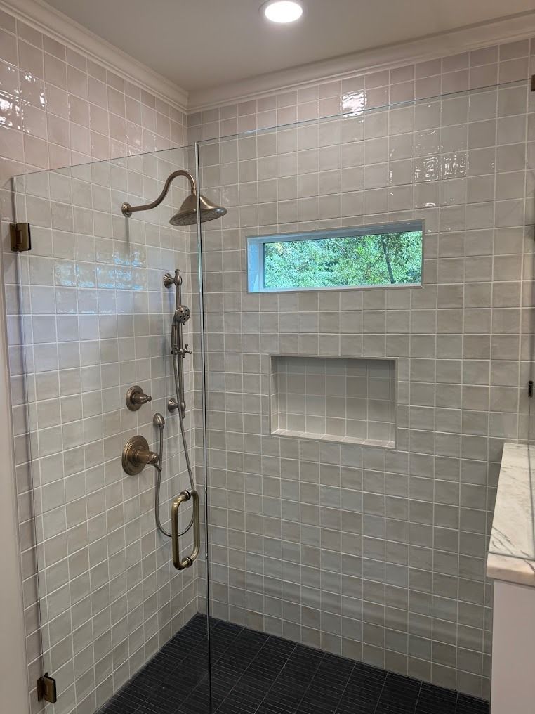 Modern tiled walk-in shower with chrome fixtures, rainfall head, built-in niches, and a small frosted window.