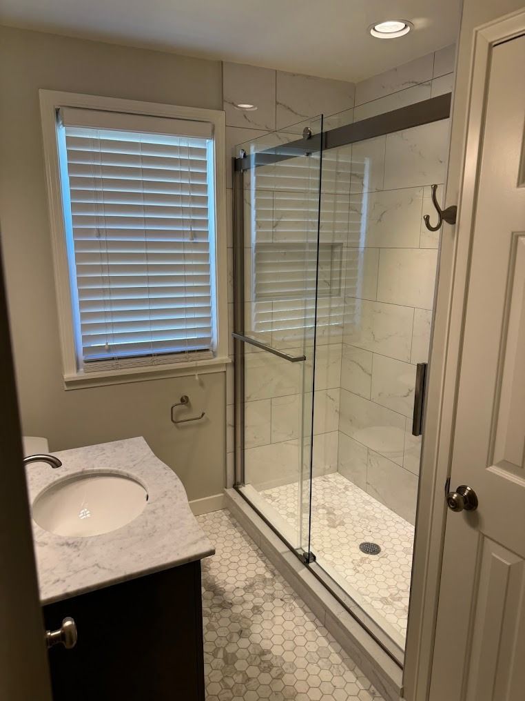 Modern bathroom with glass shower enclosure, white tile, vanity sink, and window with blinds