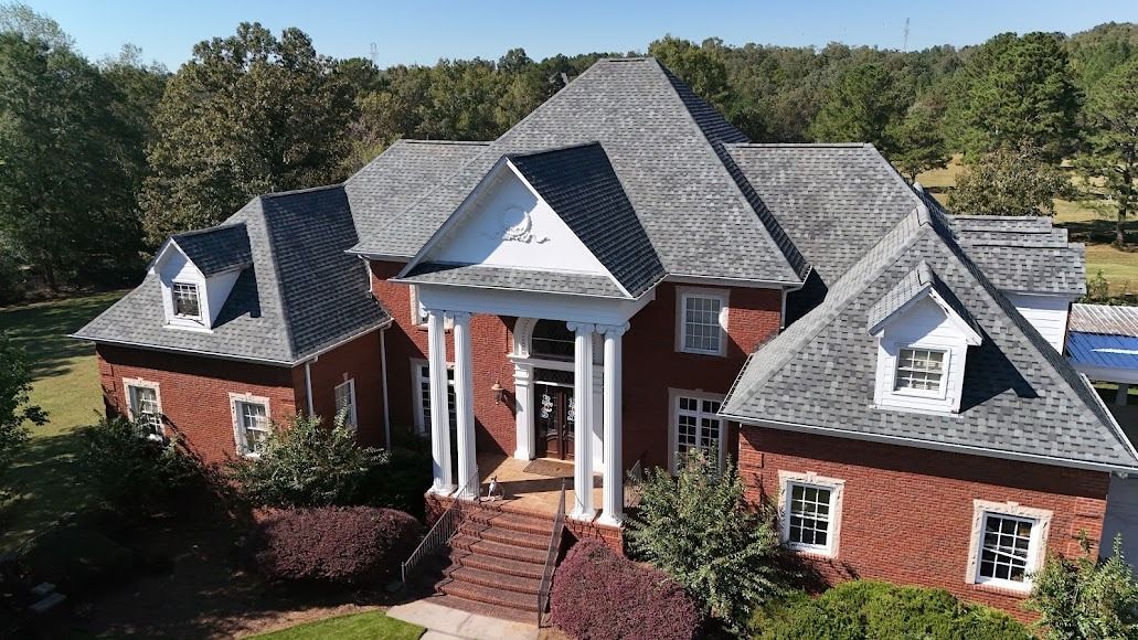 Brick house with gray gabled roof, white columns, and a front porch surrounded by trees