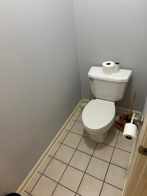 Small bathroom with a toilet, toilet paper roll, and tiled floor.