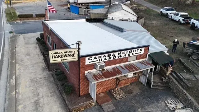 Aerial view of a brick hardware store with a metal roof, signage, and parked vehicles nearby.