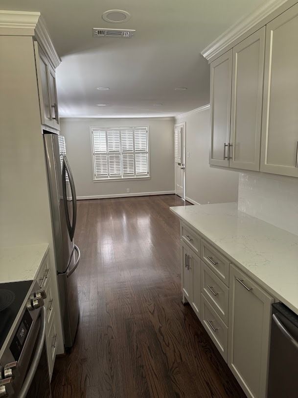 Bright kitchen with white cabinets and stainless appliances opening to a sunlit room with wood floors.
