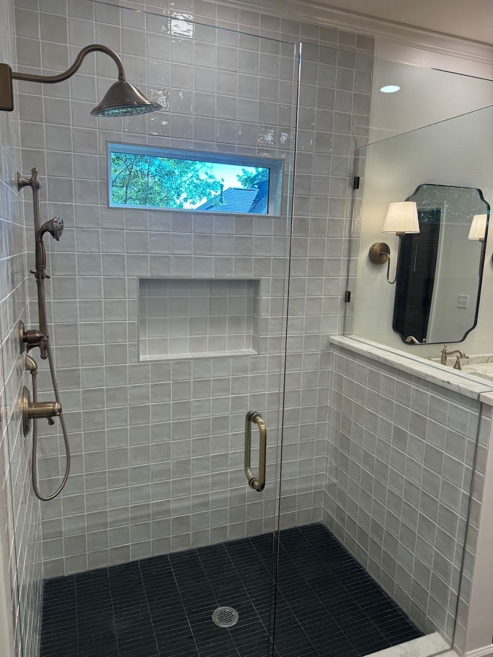 Modern bathroom shower with tiled walls, black floor, glass door, and rain showerhead.