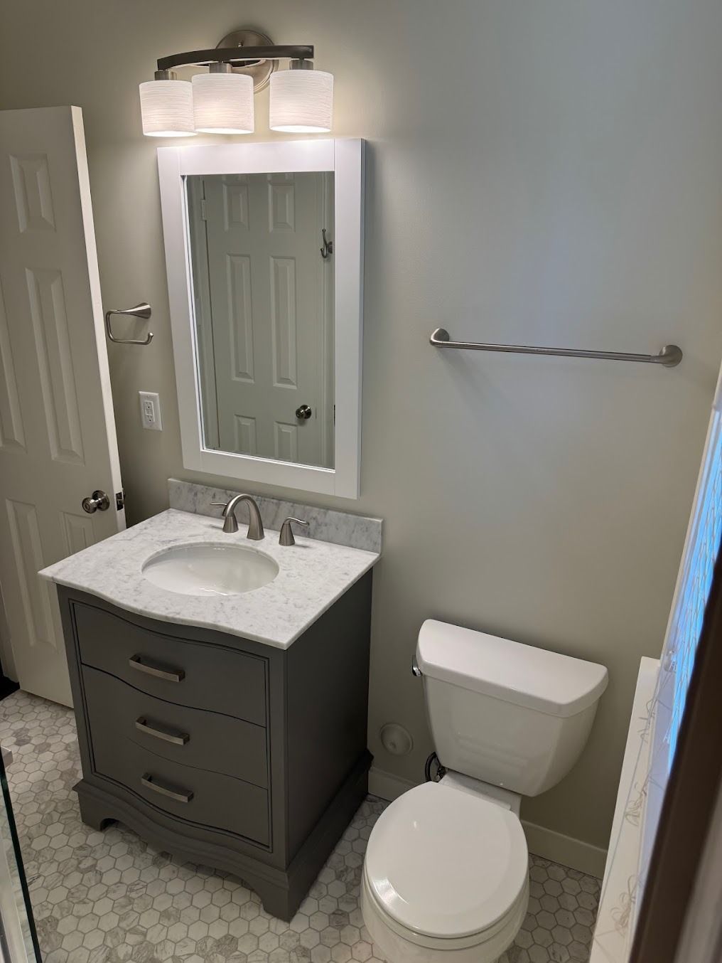Small bathroom with gray vanity, mirror, sink, toilet, and towel bar on a light wall.