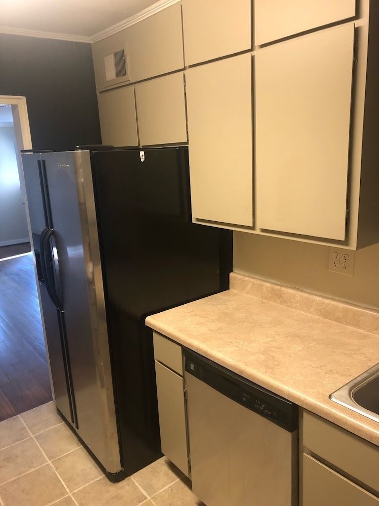 Small kitchen with black refrigerator, beige cabinets, countertop, and sink on the right.