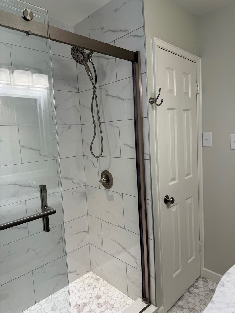 Modern bathroom with glass shower, marble tile, and a white door.