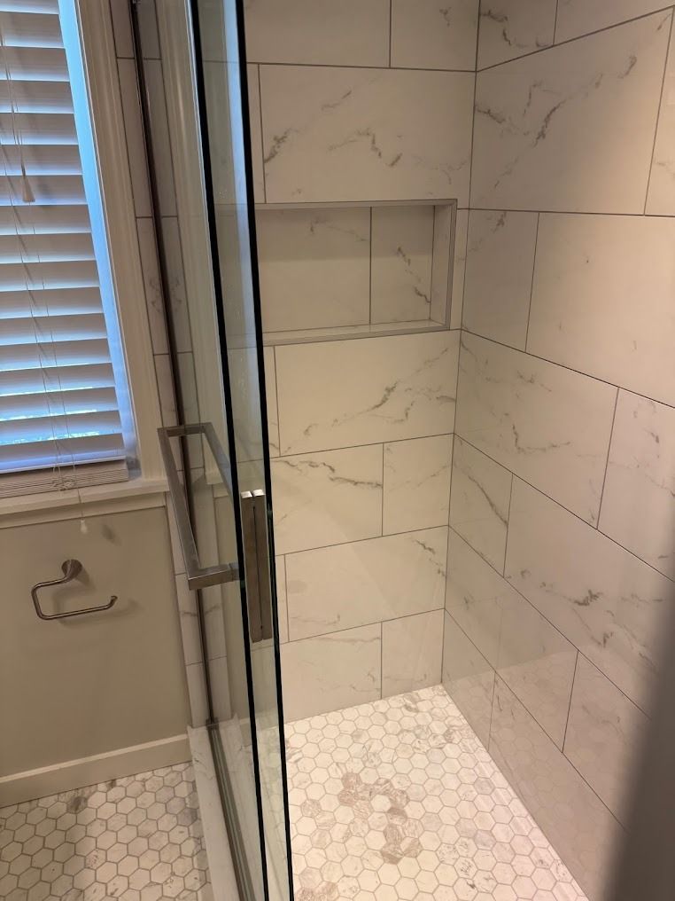 Glass shower stall with white subway tile and hex tile floor beside a window.