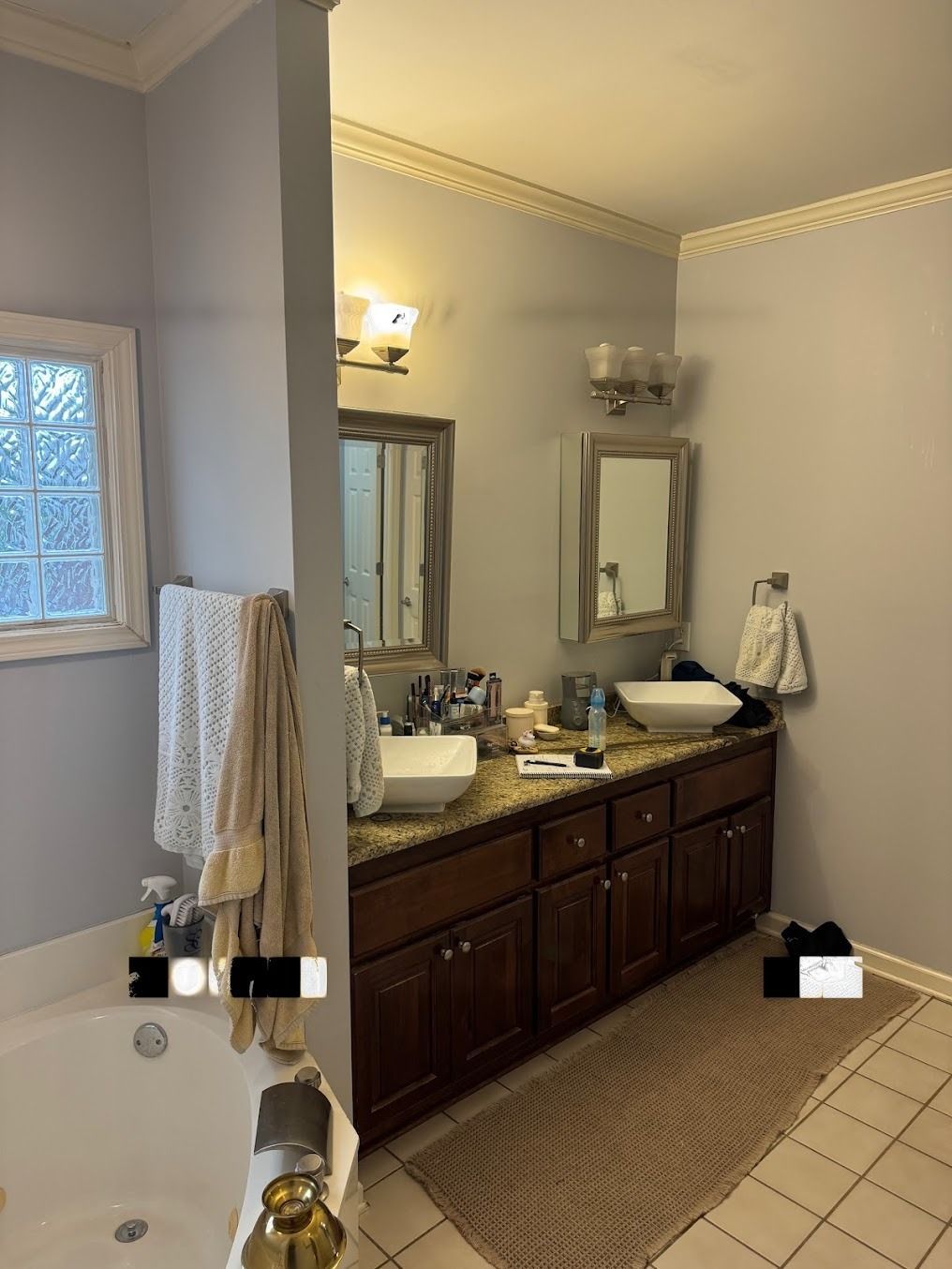 Bathroom with dark wood vanity, mirror, wall sconce, and a tiled floor beside a bathtub.