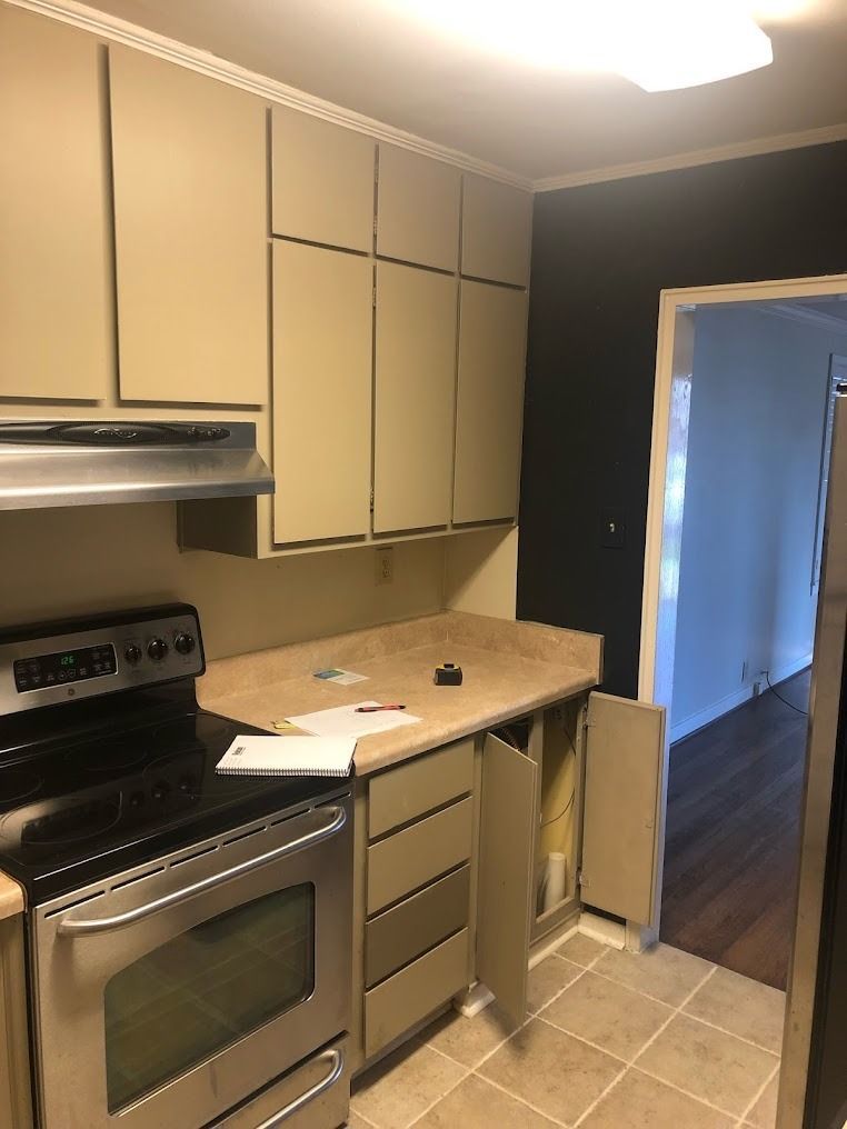 Small kitchen with beige cabinets, black stove, tan countertop, and a doorway to another room.