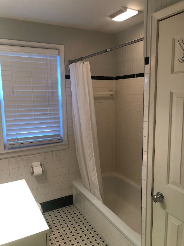 Bathroom with tub-shower, white curtain, tiled walls, window blinds, and black-and-white floor tiles