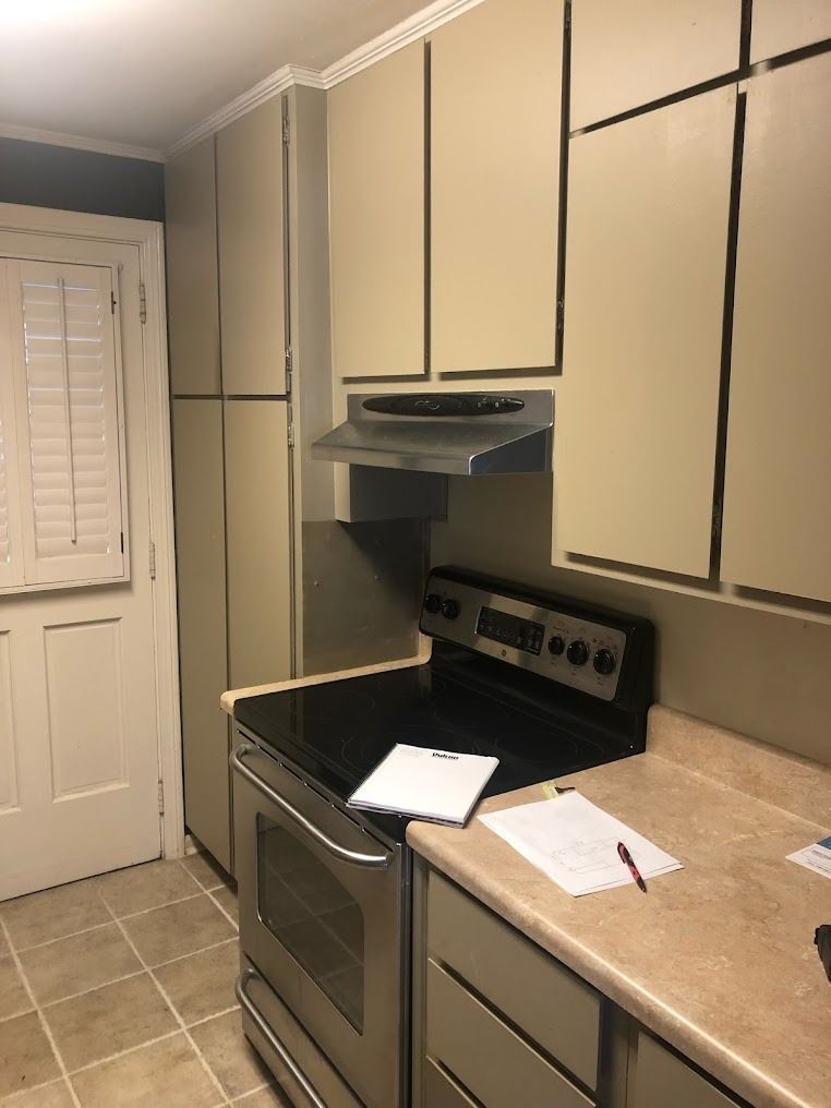 Small kitchen with beige cabinets, stove, countertop, and a door with blinds.