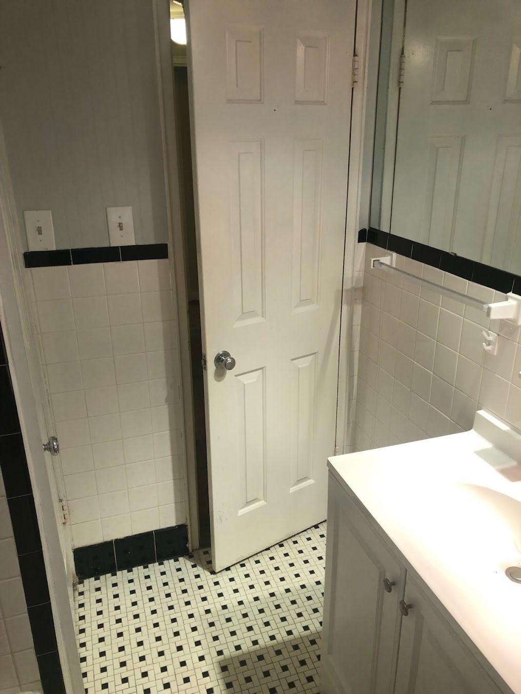 Small bathroom with white door, black trim, tiled floor, and sink counter on the right