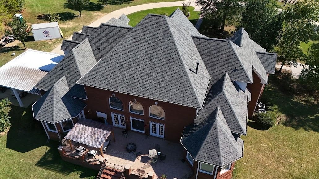 Aerial view of a large brick house with gray roof, patio, and surrounding trees