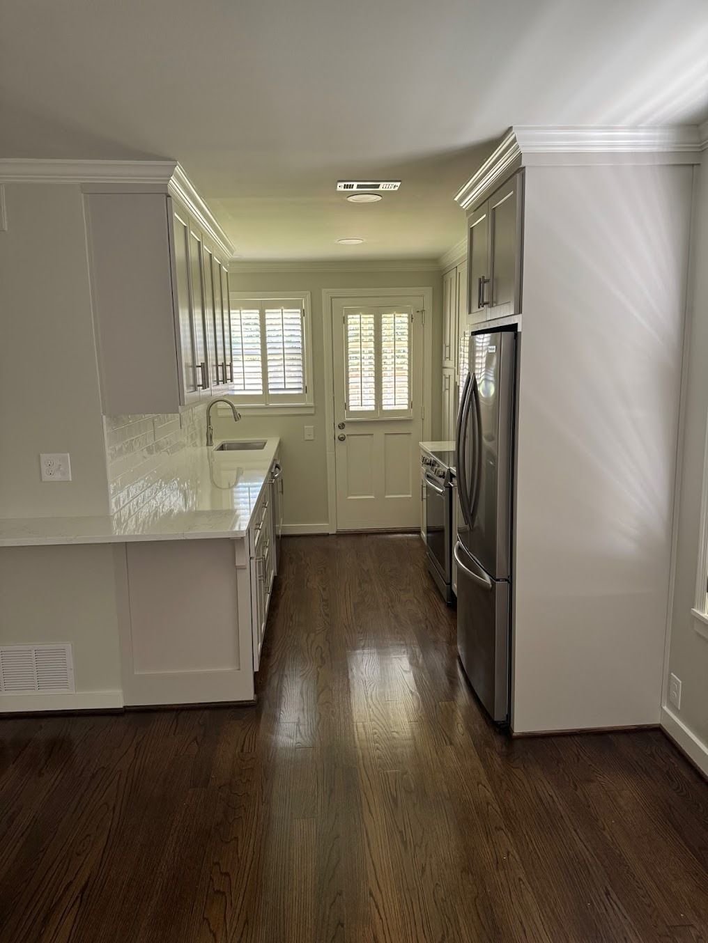 Bright kitchen with white cabinets, dark wood floors, stainless fridge, and back door with windows.