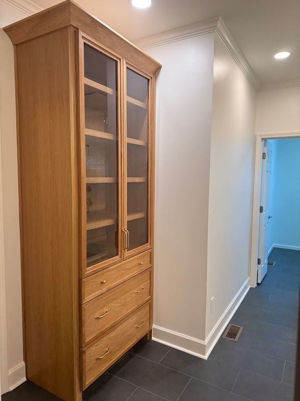 Tall wooden cabinet with glass doors and drawers in a bright hallway.