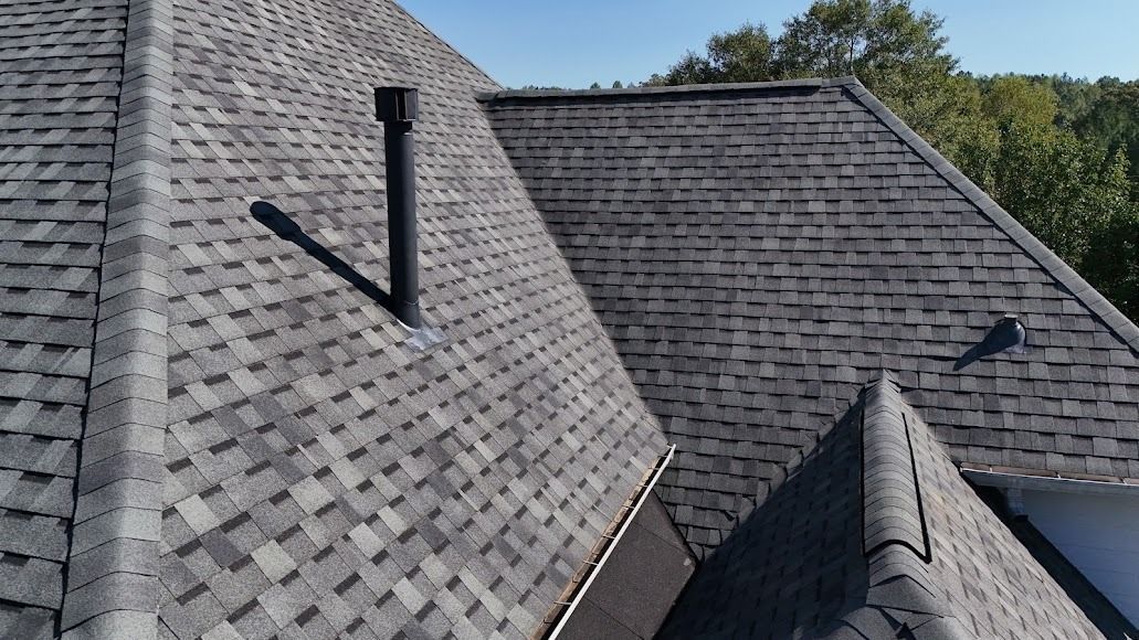Gray shingled roof slopes with black vent pipes under a blue sky