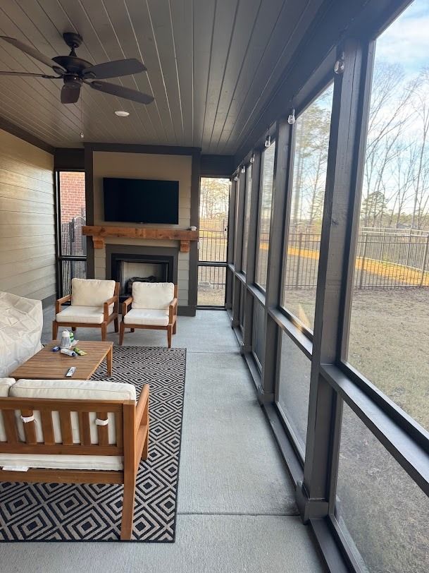 Screened porch with ceiling fan, fireplace, wicker chairs, and patterned rug overlooking a yard.